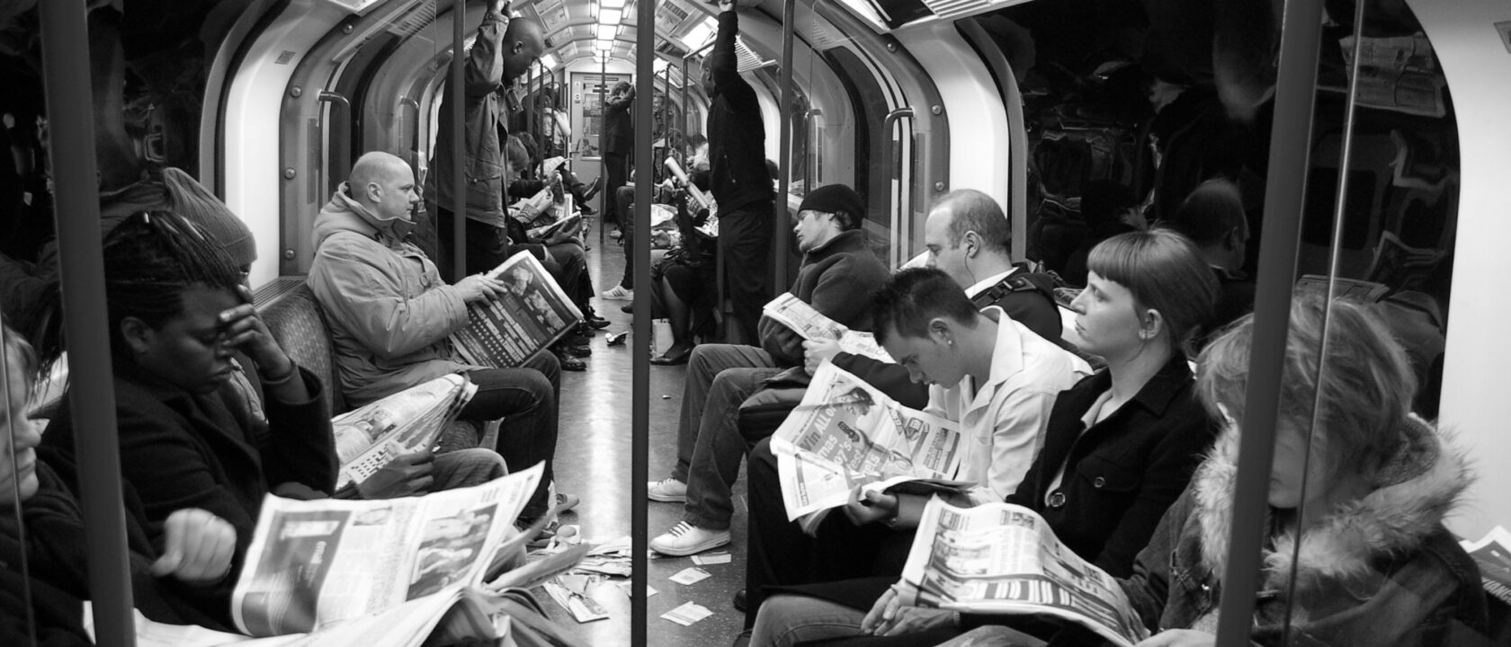 A group of people reading a newspaper on the subway.