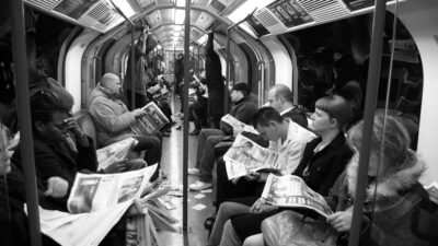 A group of people reading a newspaper on the subway.